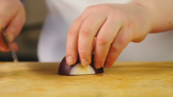 Side view cook cuts red onion into half rings on wooden chopping board — Stock Video
