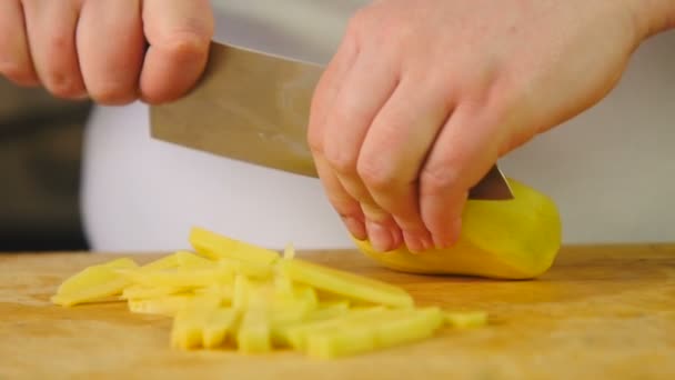Side view woman cook cuts potatoes into slices on a wooden cutting board — Stock Video