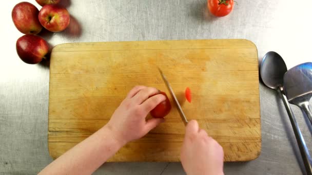 Bovenaanzicht cook snijdt tomaat in plakjes op een snijplank — Stockvideo