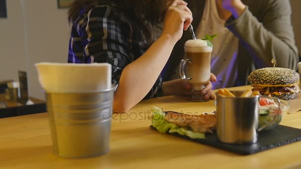 Jovem casal sentado a uma mesa em que estão hambúrgueres café e salada — Vídeo de Stock