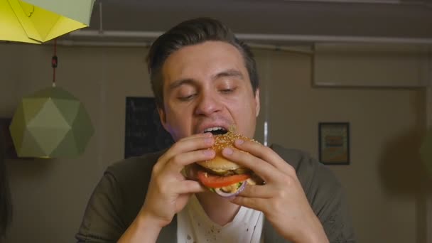 El hombre muerde y come hamburguesas en un restaurante — Vídeo de stock