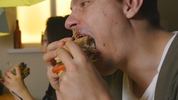 Ближче людина кусає і їсть бургер в кафе — стокове відео