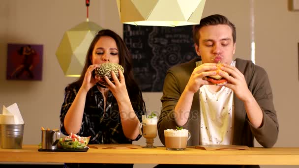 Bonita pareja come hamburguesas sentada en una mesa en un café — Vídeos de Stock