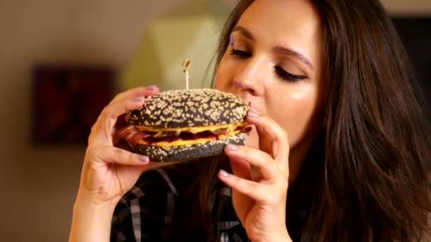 Hermosa mujer muerde y come hamburguesa en un café — Vídeos de Stock
