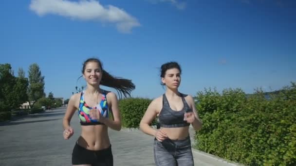 Két sport fiatal nő sportruházat futnak végig a rakparton — Stock videók