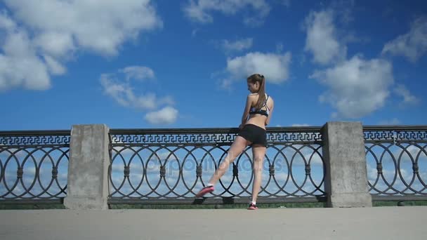 Sportif kız bacaklar çit boyunca boş sokakta germe — Stok video