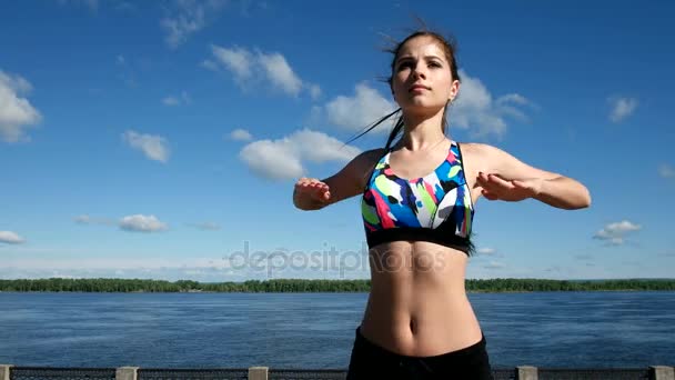 Athletic pretty girl in sports top and shorts do a body stretching on the embankment — Stock Video