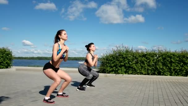 Sports pretty women in sportswear squat on the embankment — Stock Video