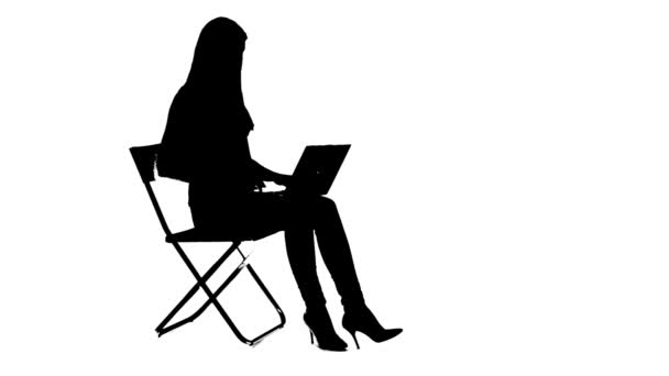 Девушка сидит на стуле и использует силуэт ноутбука — стоковое видео