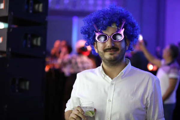 Young man wearing a blue toupee during the eighties party.