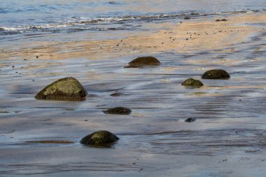 Deniz kıyısında sakin güneşli havalarda koyu volkanik kum, siyah taşlar. 