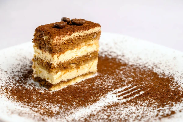 Slice of tiramisu cake decorated with coffee beans on top on a white plate
