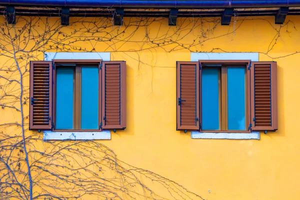 Yellow facade of a house with windows with brown shutters.