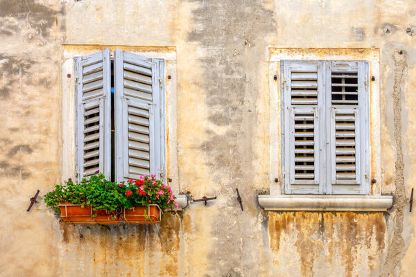 Facade of an old dirty house with blue shutters and flowers in a flowerpot