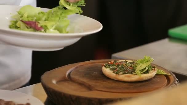 Шеф-повар кладет зеленый лист салата на бургер — стоковое видео
