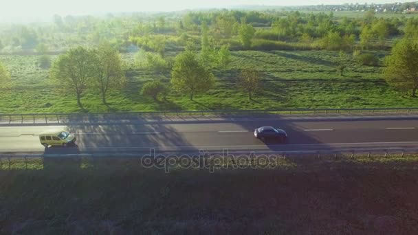 Imágenes aéreas de 4K de coches montados en una carretera entre campos verdes al amanecer — Vídeos de Stock