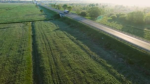 在太阳升起的绿色字段之间的道路上驾驶的白色车辆 4 k 空中观看 — 图库视频影像