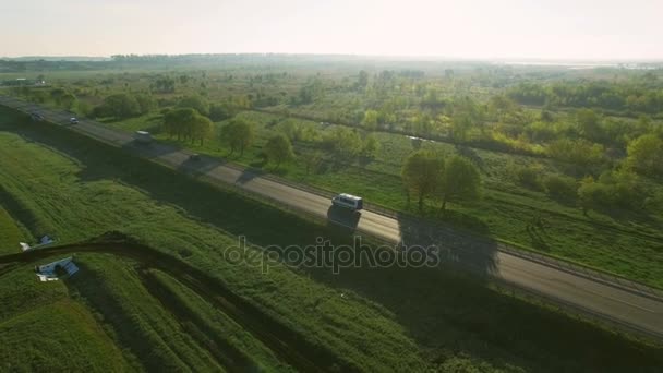 在太阳升起的绿色字段之间的道路上驾驶汽车 4 k 空中观看 — 图库视频影像