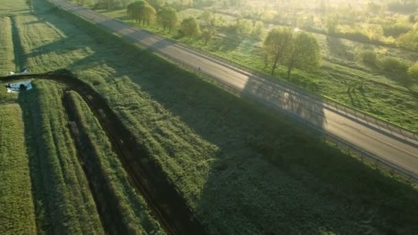 4k Luftaufnahmen eines Autos, das auf einer Straße zwischen grünen Feldern im Sonnenaufgang fährt — Stockvideo