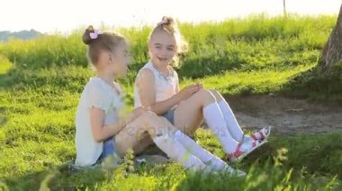 Konuşurken çimenlerin üzerinde oturan iki küçük kız iyi eğlenceler