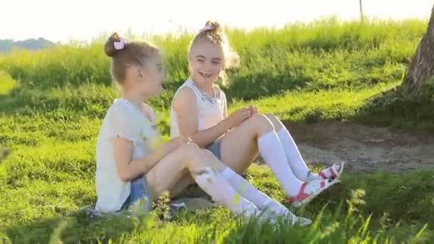 Dvě malé holčičky sedící na trávě mluví bavit — Stock video