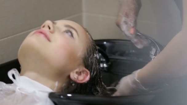 Cabeleireiro em luvas lavar o cabelo de mulheres jovens no salão — Vídeo de Stock