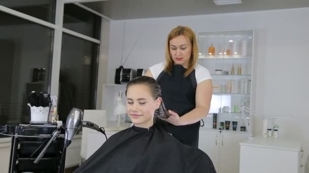 Парикмахер расчесывает волосы клиентки-подростка в парикмахерской — стоковое видео