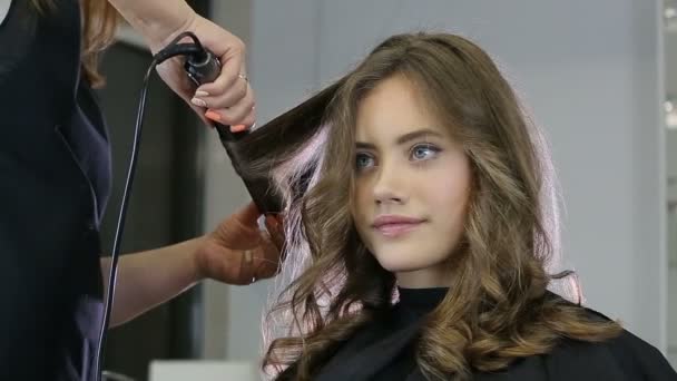 Профессиональный парикмахер скручивает волосы девушки-подростка — стоковое видео
