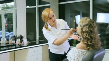 Profesyonel makyaj sanatçısı ton krem sarışın uzun curl saç ve mavi gözleri modeli cilde uygulanıyor. Yüz şekillendirme.