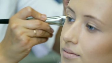 Profesyonel makyaj sanatçısı ton krem sarışın uzun curl saç ve mavi gözleri modeli cilde uygulanıyor. Yüz şekillendirme.