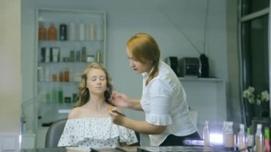 Profesyonel makyaj sanatçısı ton krem sarışın uzun curl saç ve mavi gözleri modeli cilde uygulanıyor. Yüz şekillendirme.