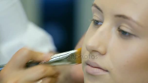 Professionele make-up artiest tonale crème op blonde lange krul haar en blauwe ogen model huid toe te passen. Vormgeven van gezicht. — Stockvideo