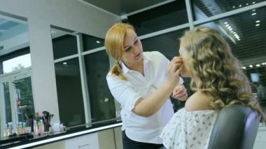 Sarışın uzun curl saç ve mavi gözleri modeli cilt için ton krem uygulayarak profesyonel makyaj sanatçısı.
