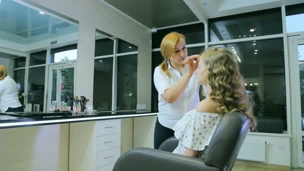 Maquilleuse professionnelle appliquant une crème tonale sur cheveux longs blonds bouclés et peau modèle aux yeux bleus . — Video