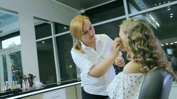 Professionele make-up artiest tonale crème op blonde lange krul haar en blauwe ogen model huid toe te passen. — Stockvideo