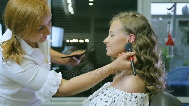 Professional makeup artist applying tonal powder to blond models skin. — Stock Video