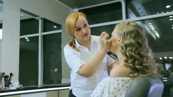 Artista de maquillaje profesional aplicando polvo tonal a modelos rubios del párpado . — Vídeos de Stock