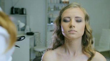 Profesyonel makyaj sanatçısı sarışın modelleri yüz whith cilt fırça temizler.