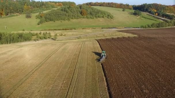 Aerial shot of tractor plowing black soil close to forest. Autumn sunset. — Stock Video