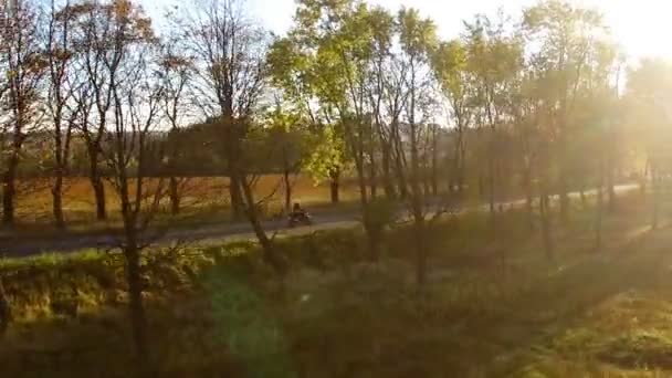 Εναέρια άποψη κοντά στο νεαρό άνδρα στο λευκό κράνος οδηγώντας μοτοσικλέτα στο φθινοπωρινό ηλιοβασίλεμα προς Δύση — Αρχείο Βίντεο