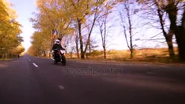 Steadycam schot van motorrijder zijn motor rijden op de weg tijdens zonsondergang — Stockvideo
