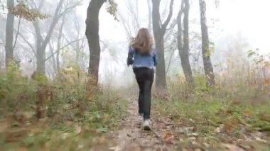 Küçük Avrupa kızla uzun saçlı, mavi ceket, siyah pantolon, spor ayakkabı ve mavi gözlü. Korkmuş küçük bir çocuk sisli ıssız ormanda çalışıyor. Yalnızlık.