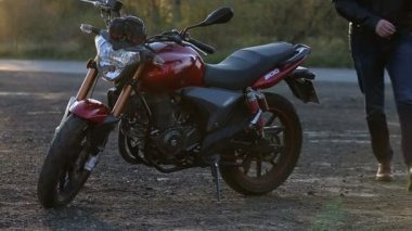 Beyaz kask ile siyah deri ceketli genç bir adam onun motosiklet için gider ve üzerinde yolculuk sonbahar gün batımında önce oturur