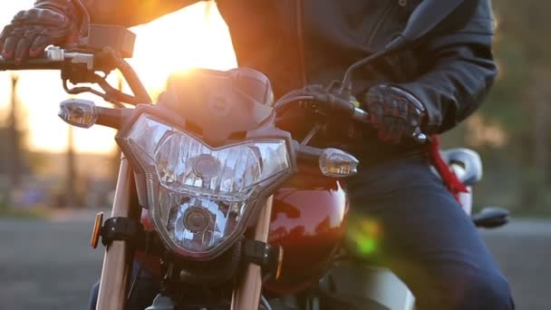 Молодий чоловік в чорній шкіряній куртці і білому шоломі сидить на мотоциклі вмикає світло перед поїздкою на осінній захід сонця — стокове відео