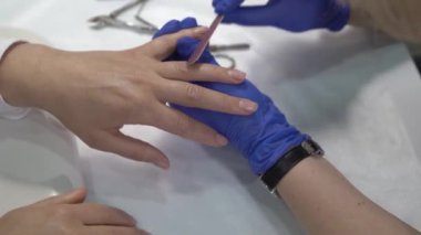 Cila sürmeden önce tırnaklarını cilalayan eldivenli profesyonel manikürcü..