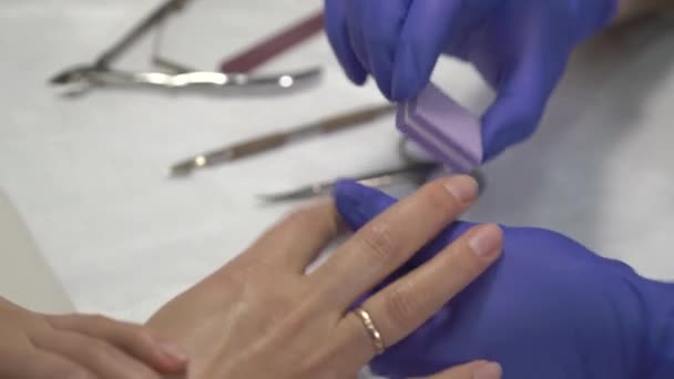 Professional manicurist in gloves polishing fingernails before covering with varnish. — Stock Video