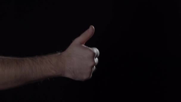 Mans hand shows humb up gesture on black background. — ストック動画