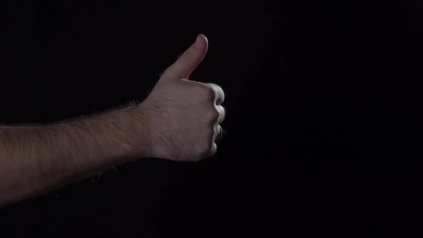 Mans hand shows thumb up gesture on black background. — Stok video