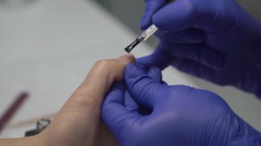 Profesyonel manikürcü, tırnaklarını şeffaf cila ile kaplıyor. Yakın çekim. 4k gerçek zamanlı görüntü.
