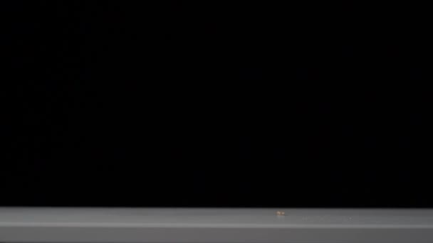 Plan au ralenti de cacahuètes tombant sur une table blanche. Fond noir .